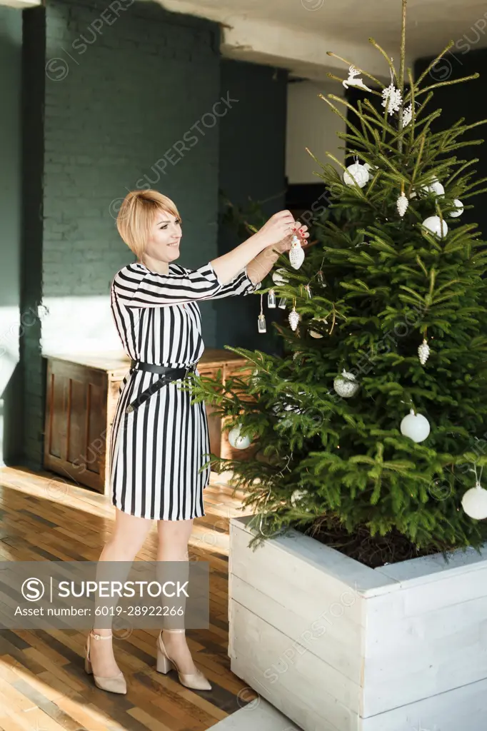 woman in a striped dress decorates a Christmas tree with ornaments