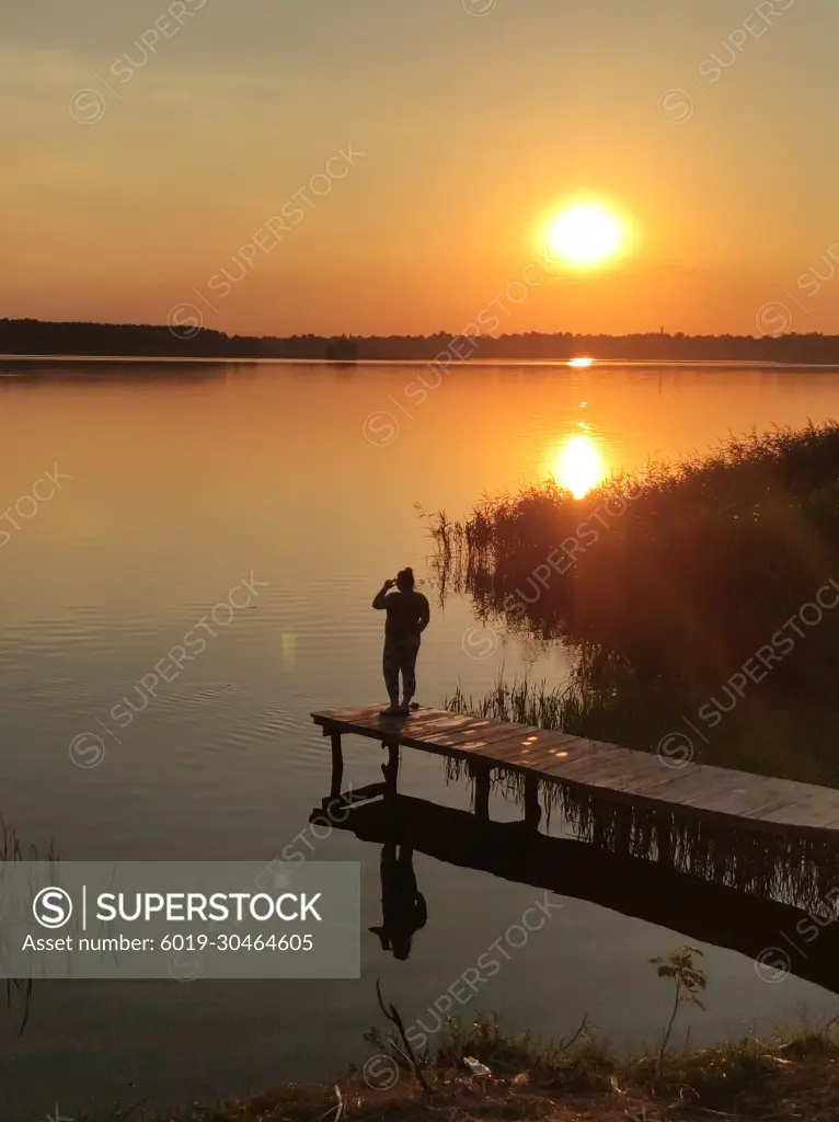 The girl admires the sunset on the bridge near the tourist lake