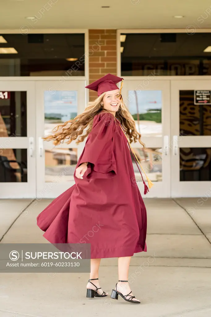 Female graduate spinning in her cap & gown in front of school doors