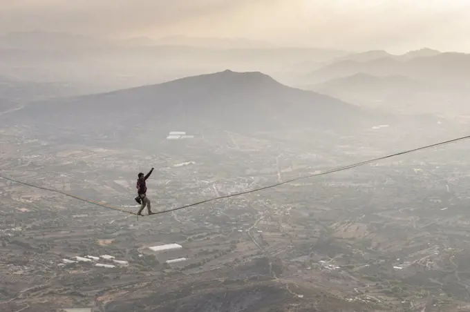 One man balancing on a highline over a valley in a mountain area