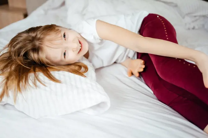 little girl laughs lying on a white bed