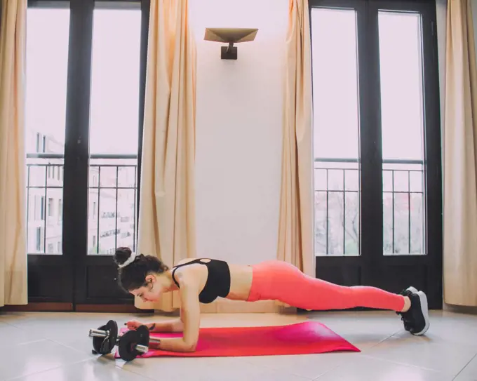 young woman exercising at home with mat and dumbbells