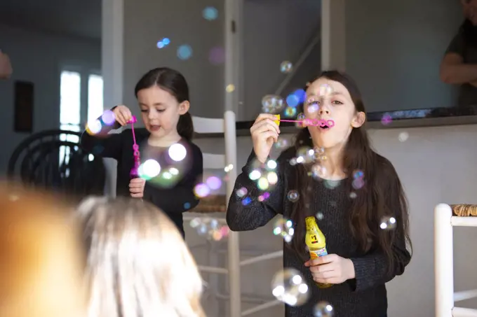 Cute little girls blowing bubbles in the kitchen with their family.