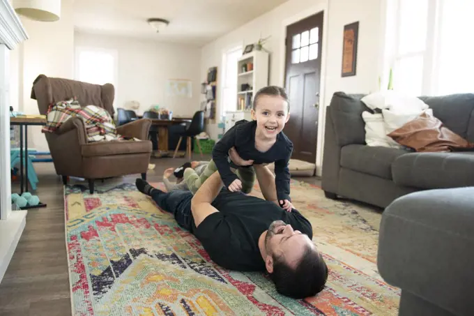 Father doing airplane with little girl on living room floor.