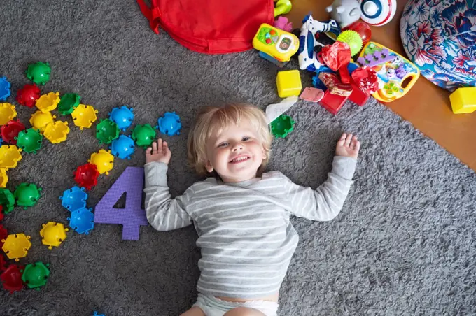 Happy blonde child lies on the floor with lots of toys