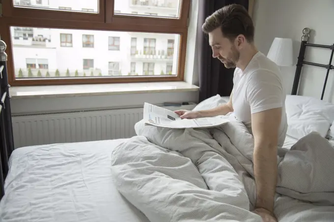 young man reading a newspaper with news in bed