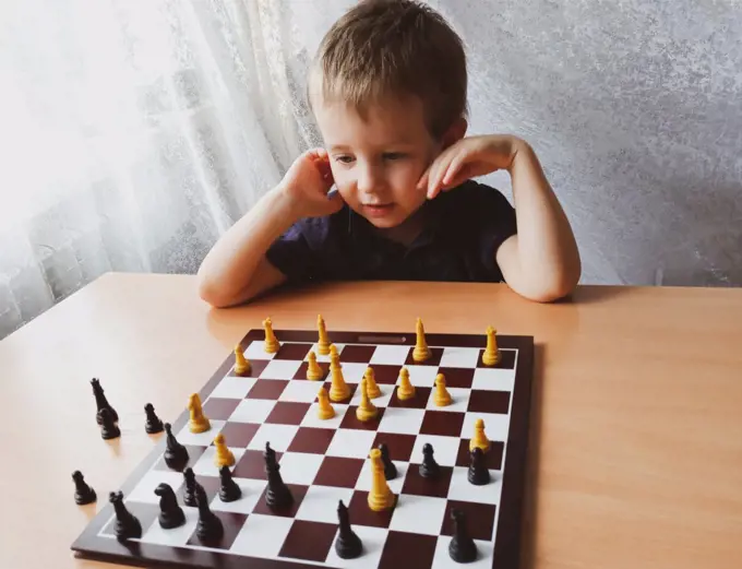 little boy thinks while playing chess at home. leisure