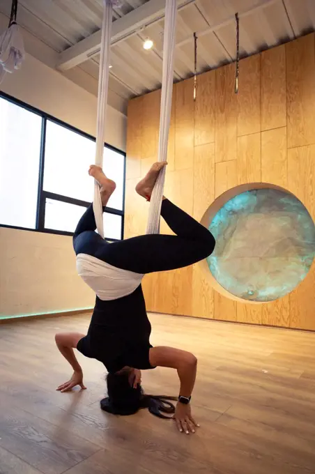 Young woman all in black doing aerial yoga at wooden studio in Mexico