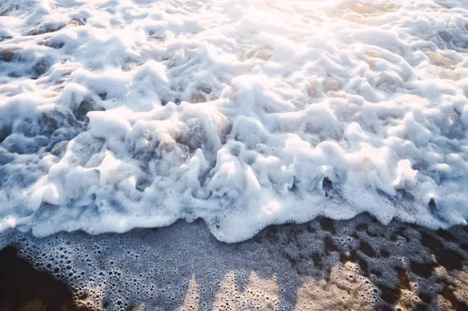 close-up of waves with sea foam against sunset