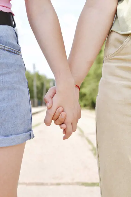 Two people hold hands on the background of the road close-up.