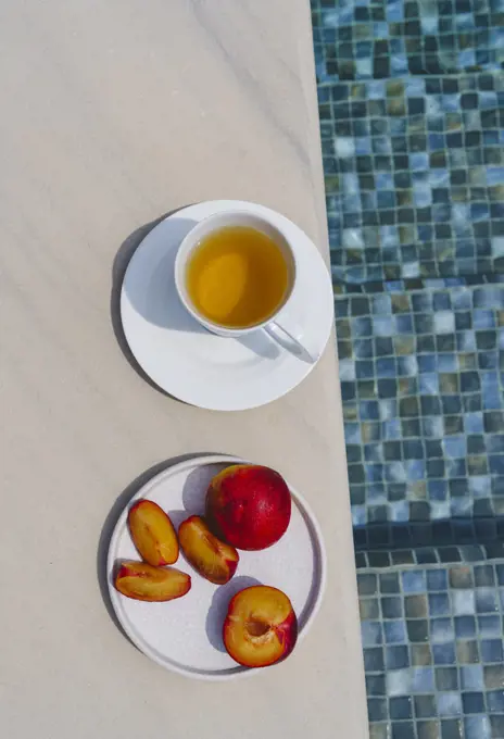 Still life, a cup of tea and a plate of peaches by the pool.