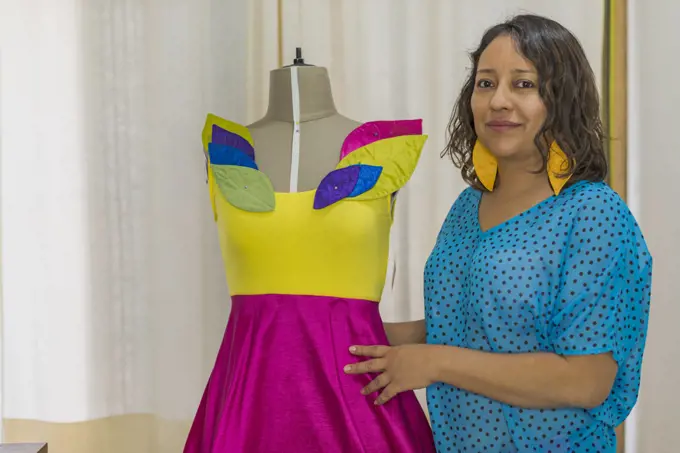 Portrait of a Latin fashion designer next to one of her creations