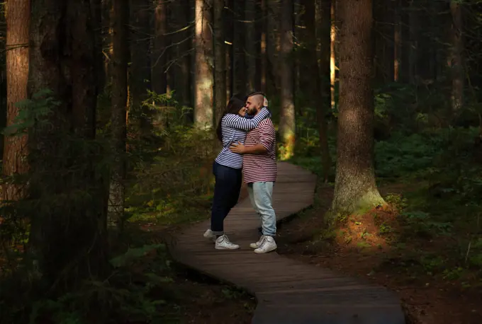 Couple in love hugging on a wooden road in a pine forest