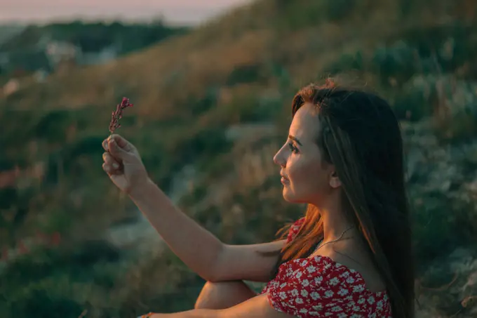 portrait of a young woman in mountains at sunset flower in her hand