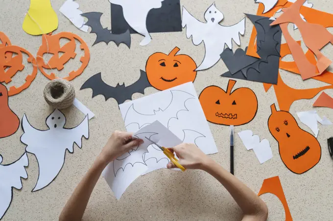 The hands of a girl with scissors make crafts for Halloween.