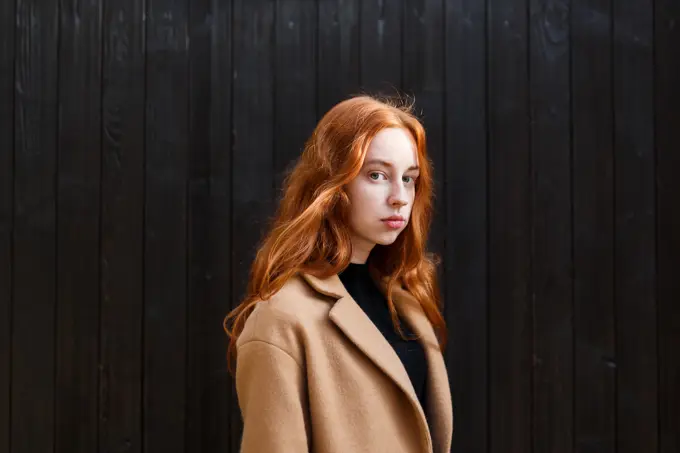 young stylish red-haired woman in a coat near her house in autumn