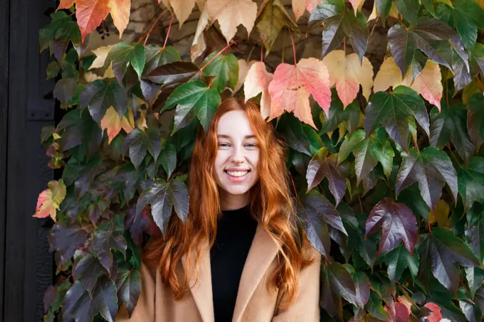 young stylish red-haired woman on the background of green leaves