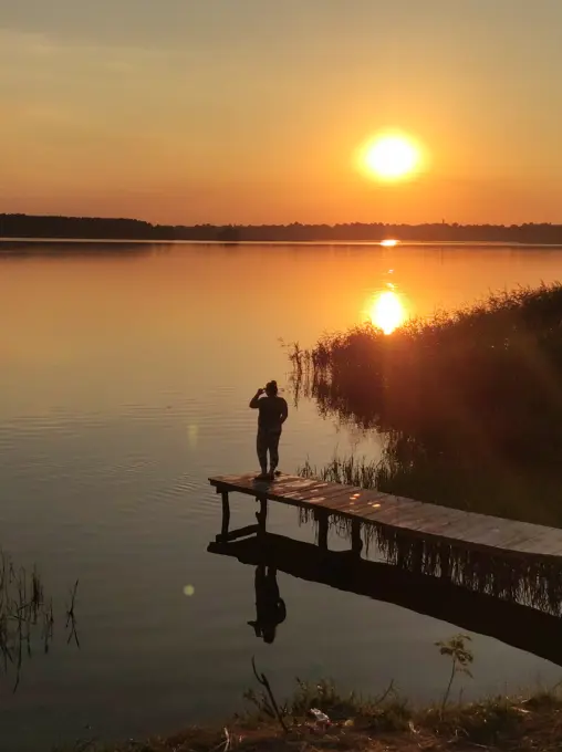 The girl admires the sunset on the bridge near the tourist lake