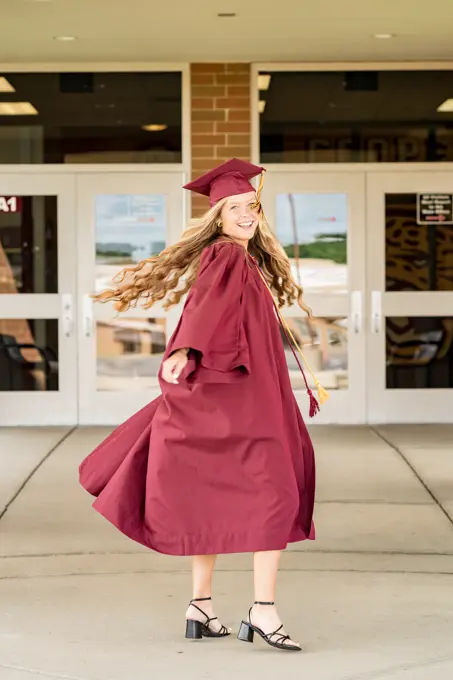 Female graduate spinning in her cap & gown in front of school doors