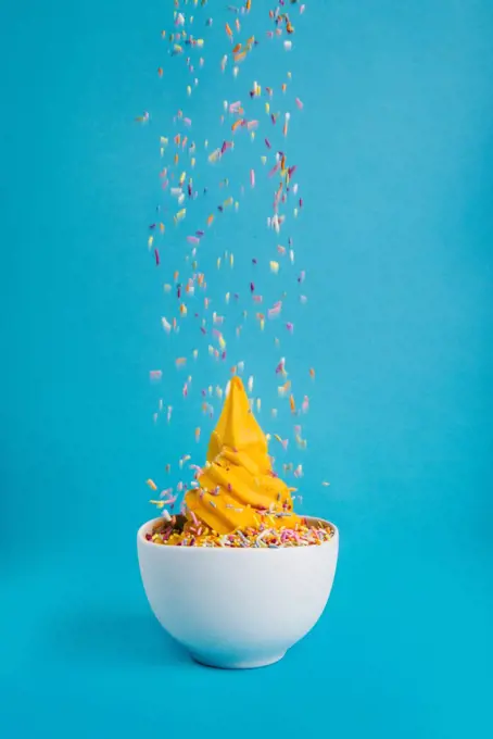 Bowl of ice cream with falling sprinkles on a blue background