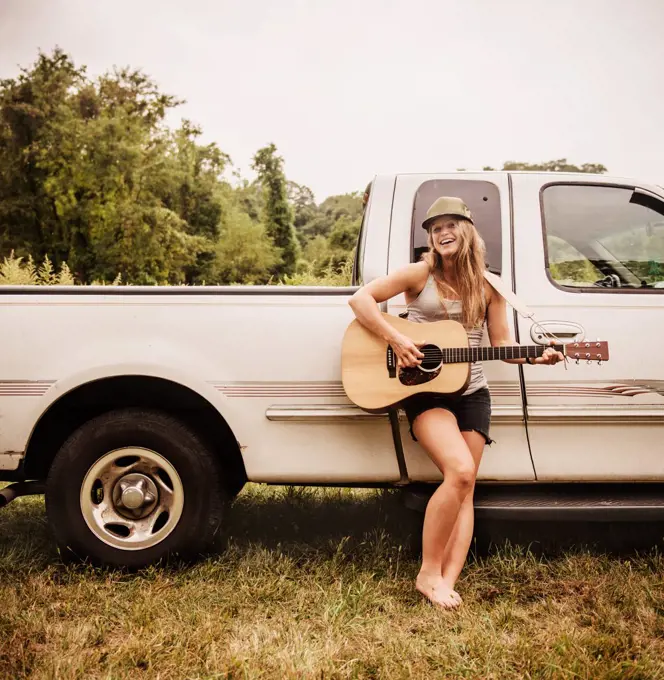 Woman playing guitar in front of her truck