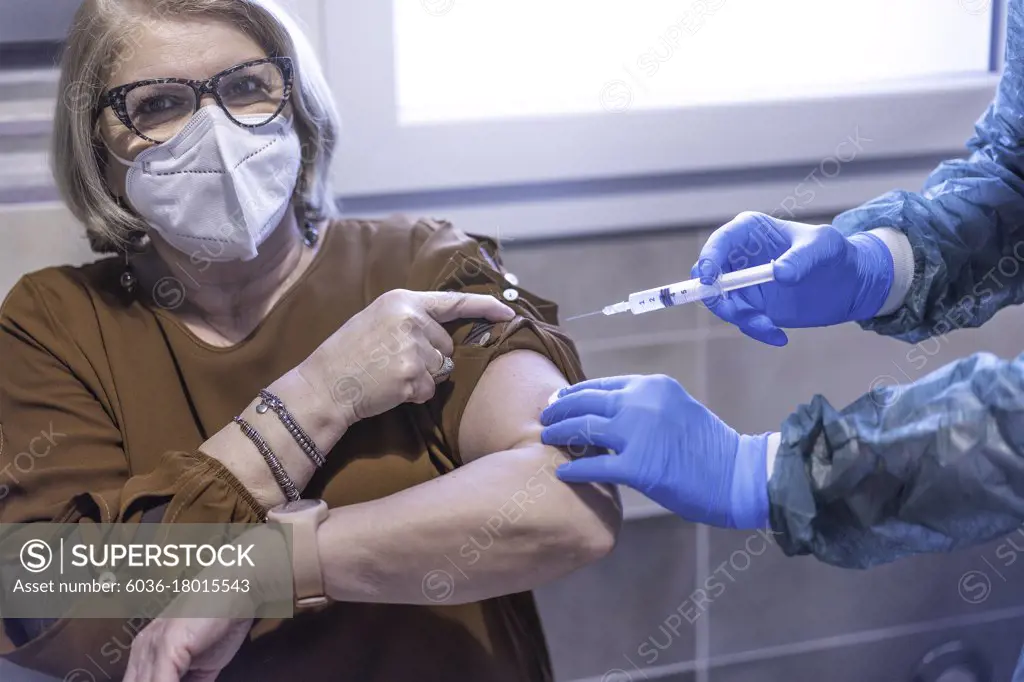 Doctor in hazmat suit giving patient a vaccine for coronavirus disease - Senior woman wearing protective face mask doing vaccine for Covid-19 illness - Medical and healthcare concept - Focus on gloves