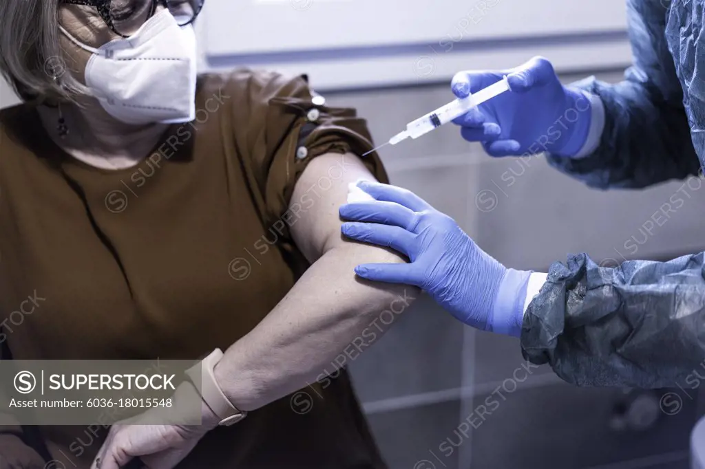 Doctor in hazmat suit giving patient a vaccine for coronavirus disease - Senior woman wearing protective face mask doing vaccine for Covid-19 illness - Medical and healthcare concept - Focus on gloves