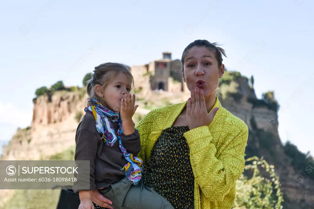 Stylish mom and daughter having fun together - Cute preschool girl and her young mother looking at camera and blowing a kiss - Mum and daughter traveling together in a beautiful destination in Italy