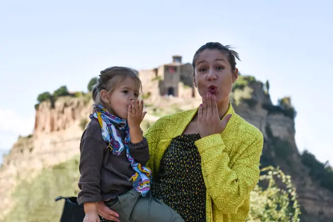 Stylish mom and daughter having fun together - Cute preschool girl and her young mother looking at camera and blowing a kiss - Mum and daughter traveling together in a beautiful destination in Italy