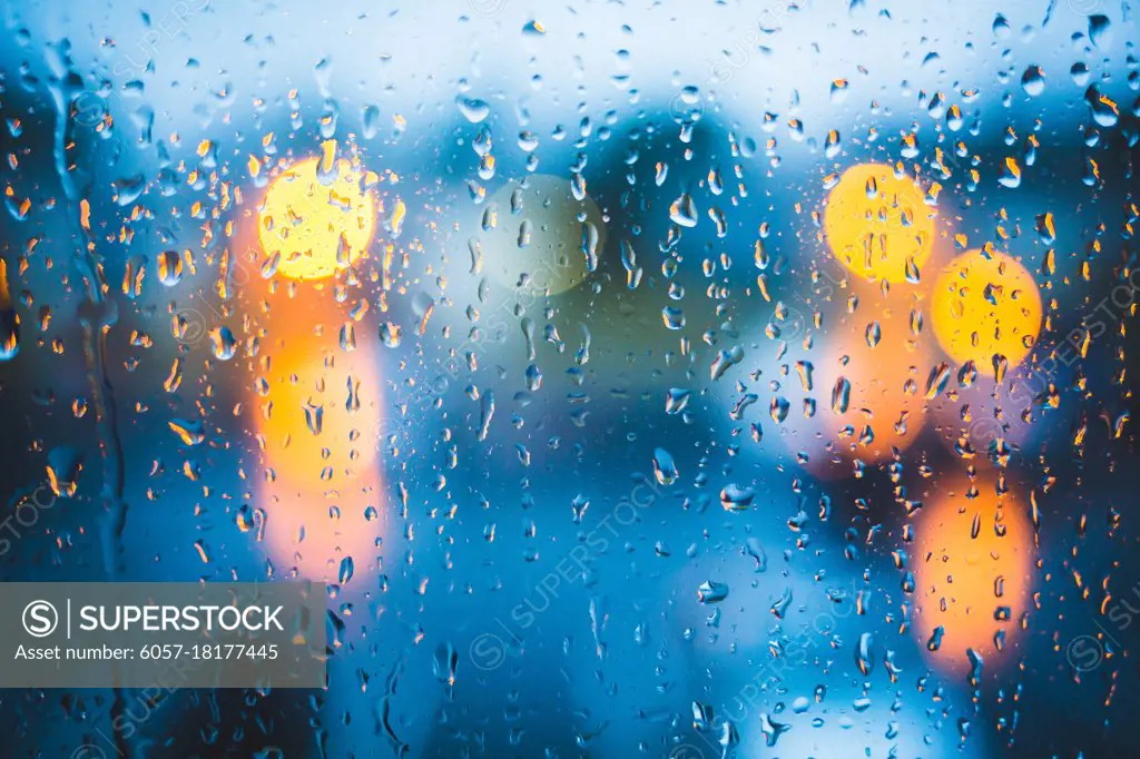 Rain drops on window. Peaceful evening or night at home when raining outside. Water drops on glass. Surface of wet glass. Water splash. City lights bokeh during the rain.