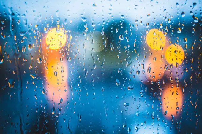 Rain drops on window. Peaceful evening or night at home when raining outside. Water drops on glass. Surface of wet glass. Water splash. City lights bokeh during the rain.