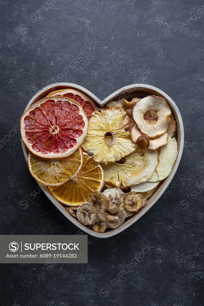 Dried fruit slices in heart shaped bowl. Dried orange, grapefruit, pineapples, banana. Healthy snack or desserts