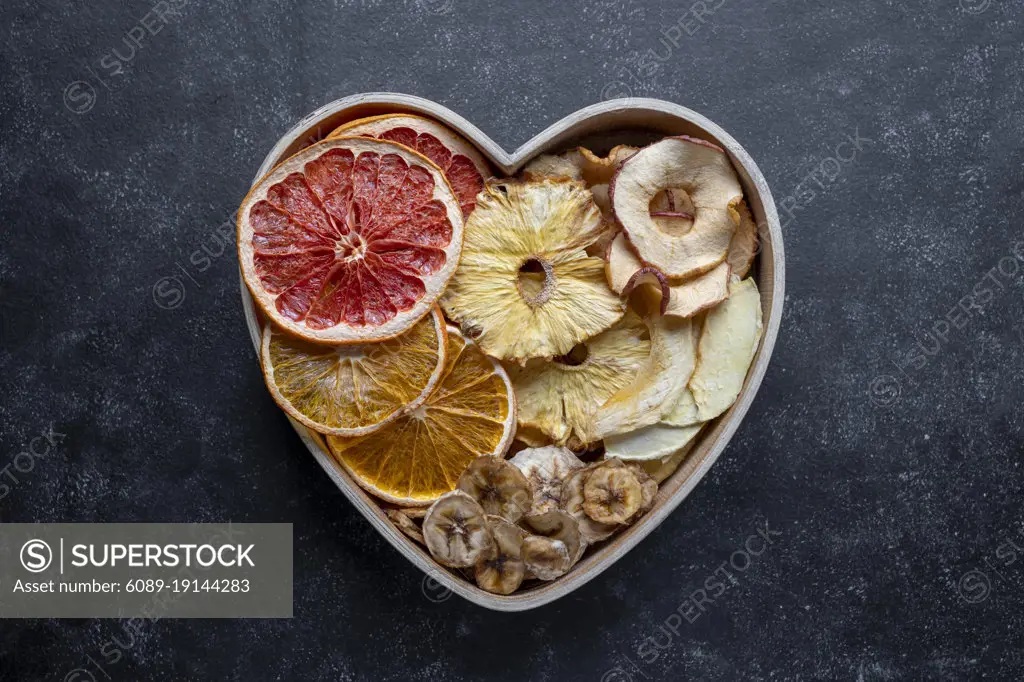 Dried fruit slices in heart shaped bowl. Dried orange, grapefruit, pineapples, banana. Healthy snack or desserts