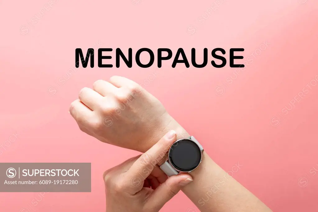 Menopause word text, hands with watch, abstract concept of time, pink background, top view