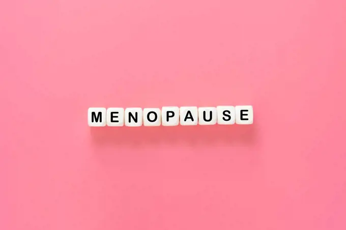 Menopause word abstract text, wooden blocks over pink background, top view