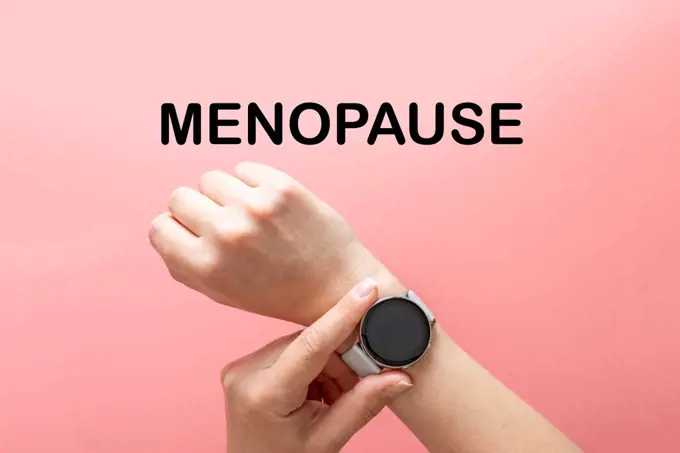 Menopause word text, hands with watch, abstract concept of time, pink background, top view