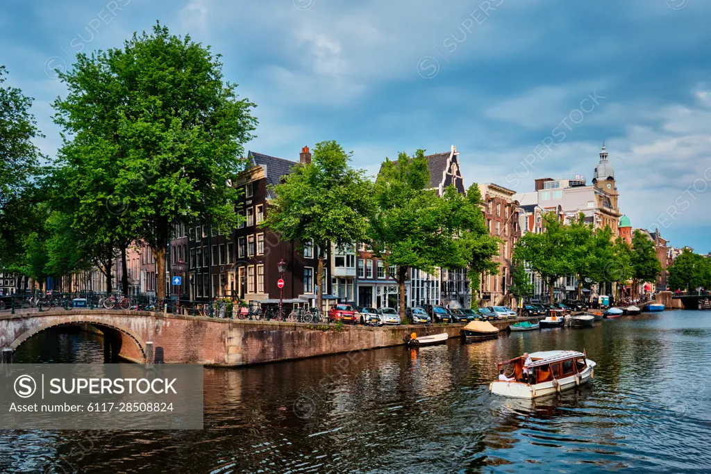 Amsterdam view - canal with tourist boat, bridge and old houses. Amsterdam, Netherlands