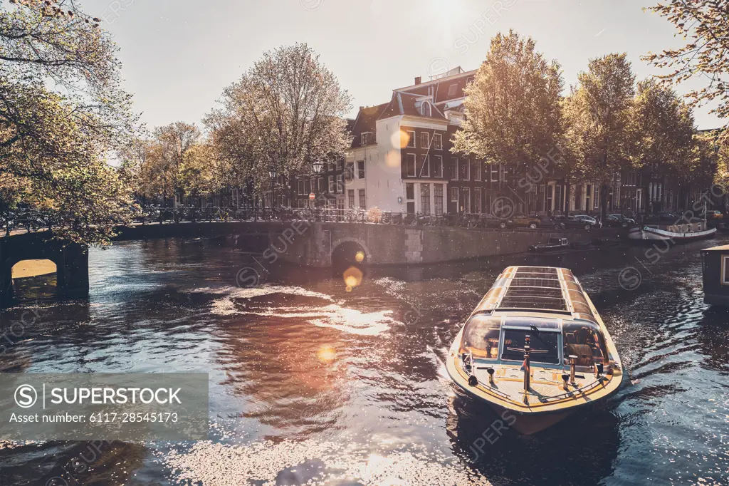 Amsterdam canal with tourist boat and old houses on sunset. Amsterda, Netherlands