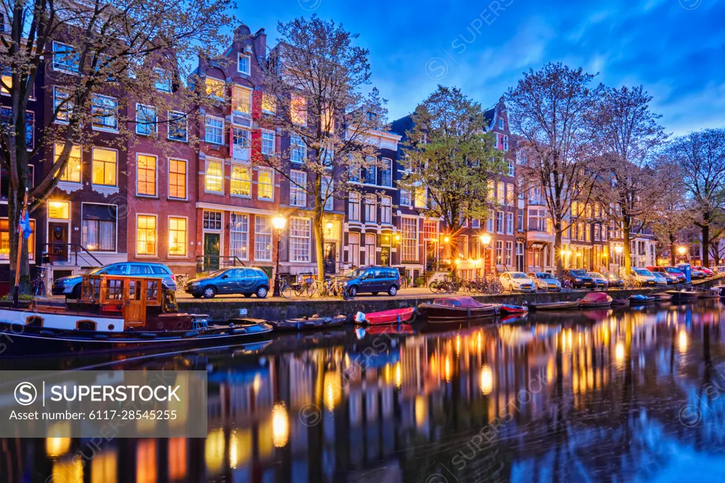 Night view of Amsterdam cityscape with canal, boats and medieval houses in the evening twilight illuminated. Amsterdam, Netherlands