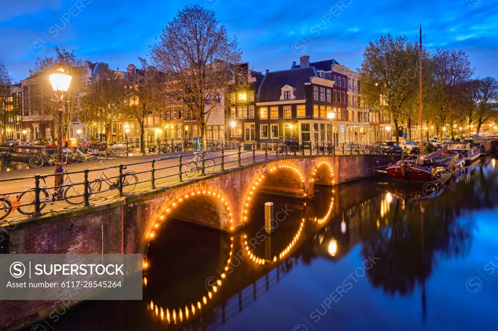 Night view of Amsterdam cityscape with canal, bridge and medieval houses in the evening twilight illuminated. Amsterdam, Netherlands