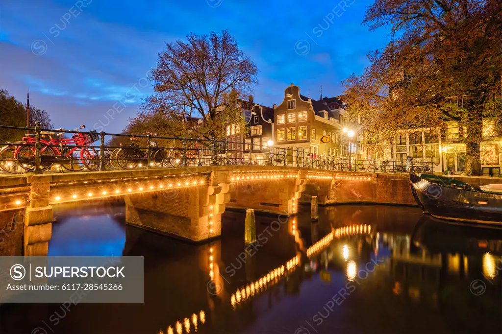 Night view of Amsterdam cityscape with canal, bridge and medieval houses in the evening twilight illuminated. Amsterdam, Netherlands