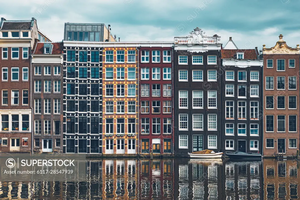 Row of typical houses and boat on Amsterdam canal Damrak with reflection. Amsterdam, Netherlands