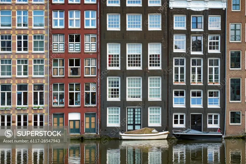 Row of typical houses and boat on Amsterdam canal Damrak with reflection. Amsterdam, Netherlands