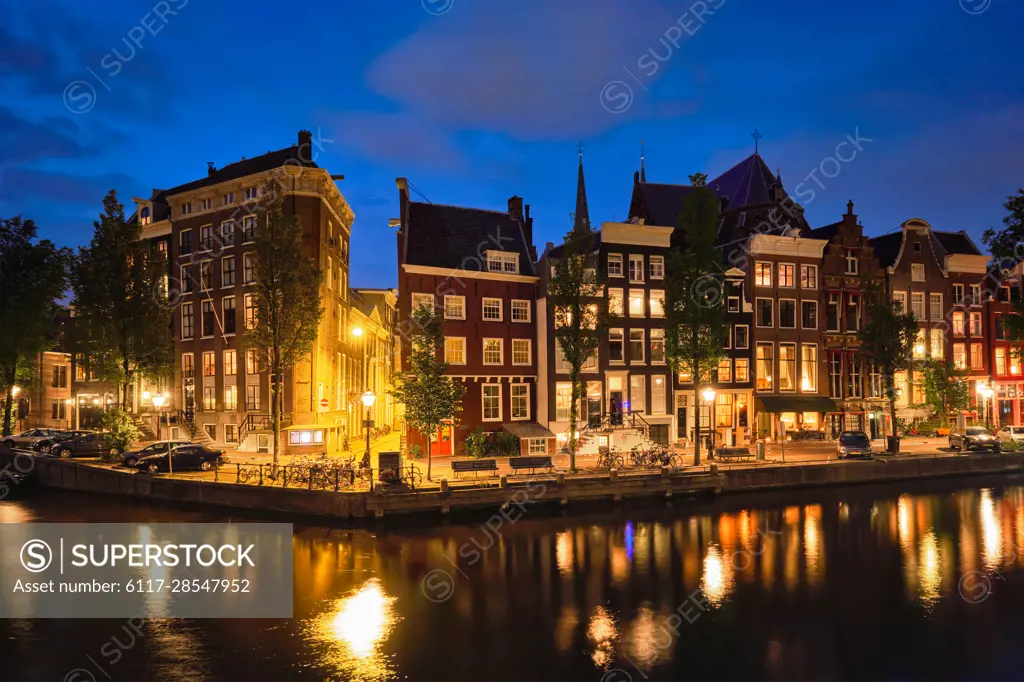 Night view of Amsterdam cityscape with canal and medieval houses in the evening twilight illuminated. Amsterdam, Netherlands