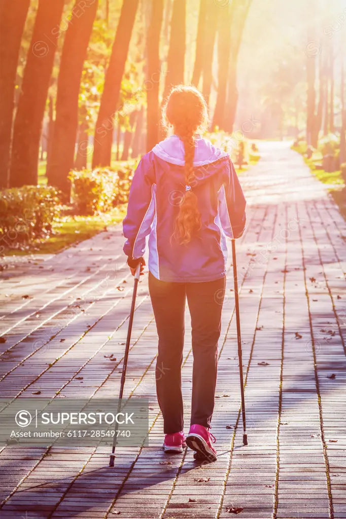 Nordic walking adventure and exercising concept - woman hiking with nordic walking poles in park. With lens flare and light leak