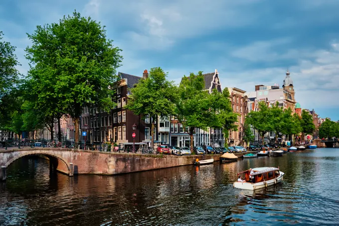 Amsterdam view - canal with tourist boat, bridge and old houses. Amsterdam, Netherlands