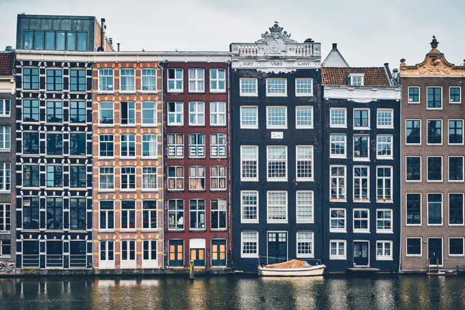 Row of typical houses and boat on Amsterdam canal Damrak with reflection. Amsterdam, Netherlands