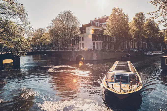 Amsterdam canal with tourist boat and old houses on sunset. Amsterda, Netherlands