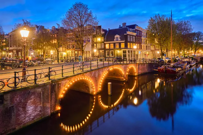 Night view of Amsterdam cityscape with canal, bridge and medieval houses in the evening twilight illuminated. Amsterdam, Netherlands