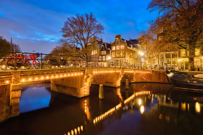 Night view of Amsterdam cityscape with canal, bridge and medieval houses in the evening twilight illuminated. Amsterdam, Netherlands